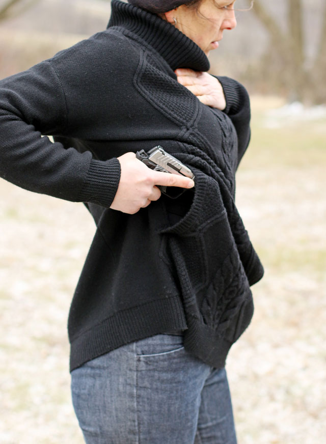Right-side view of a woman drawing a pistol from concealment of black sweater.