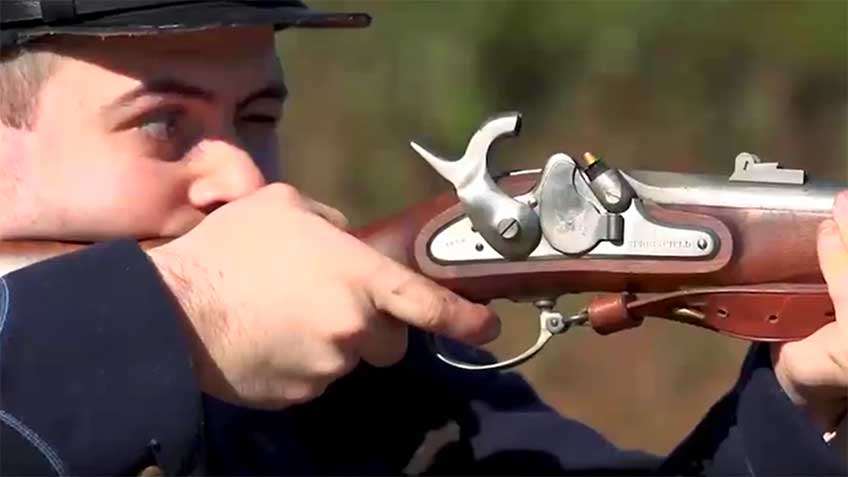 Man in vintage uniform shooting a U.S. Model 1855 Rifle-Musket with hammer cocked on sunny day.