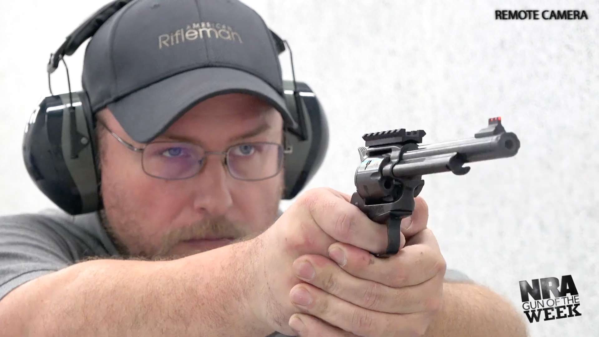 man wearing protective gear ear muffs glasses hat shooting black revolver white range walls