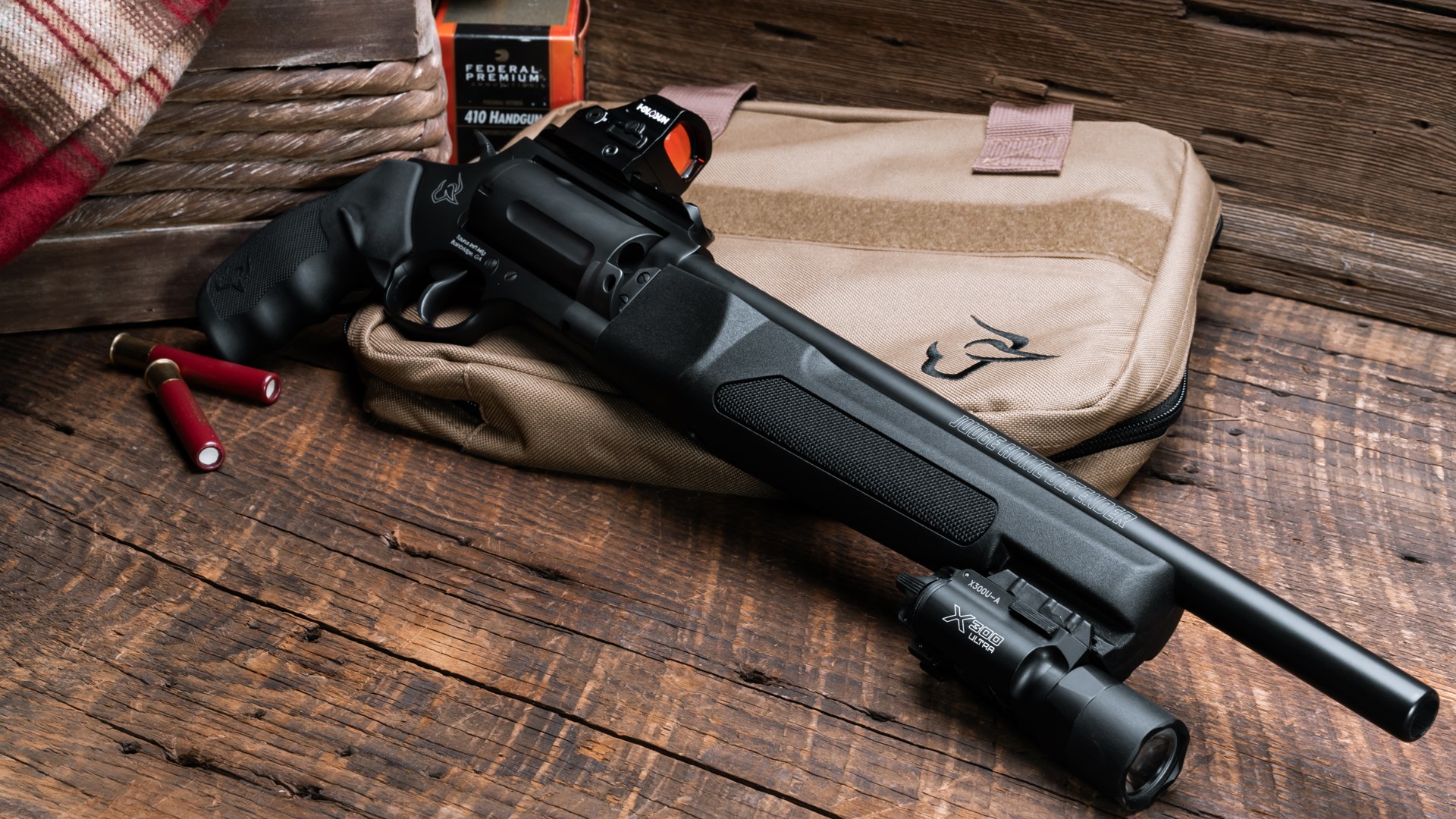 The Taurus Judge Home Defender lays on a tan bag, with a flashlight and optic mounted.