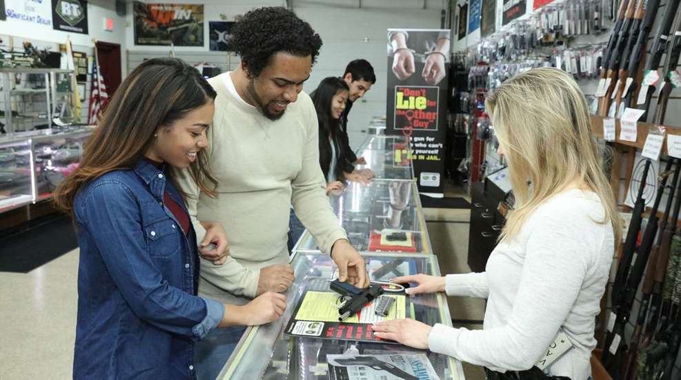 People at gun counter looking at pistol three women two men