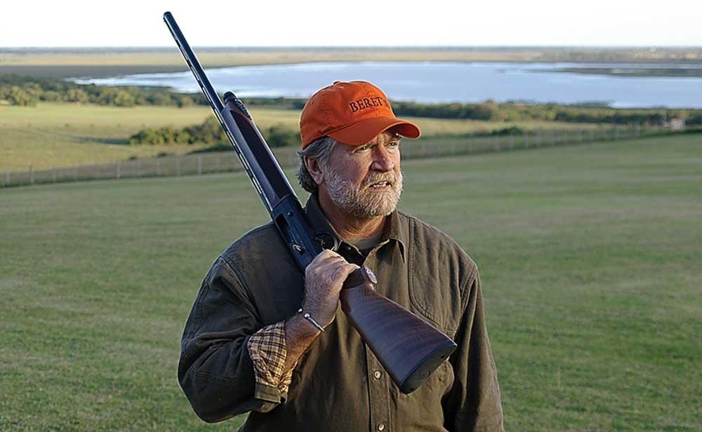 Author man with Beretta shotgun hunting outdoors field lake
