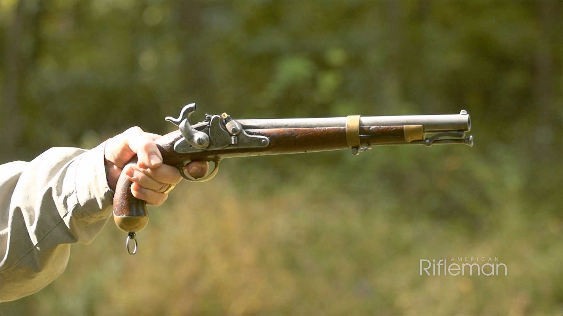 Man aiming the U.S. Model 1855 pistol carbine without a shoulder stock attached against a green, outdoors background.
