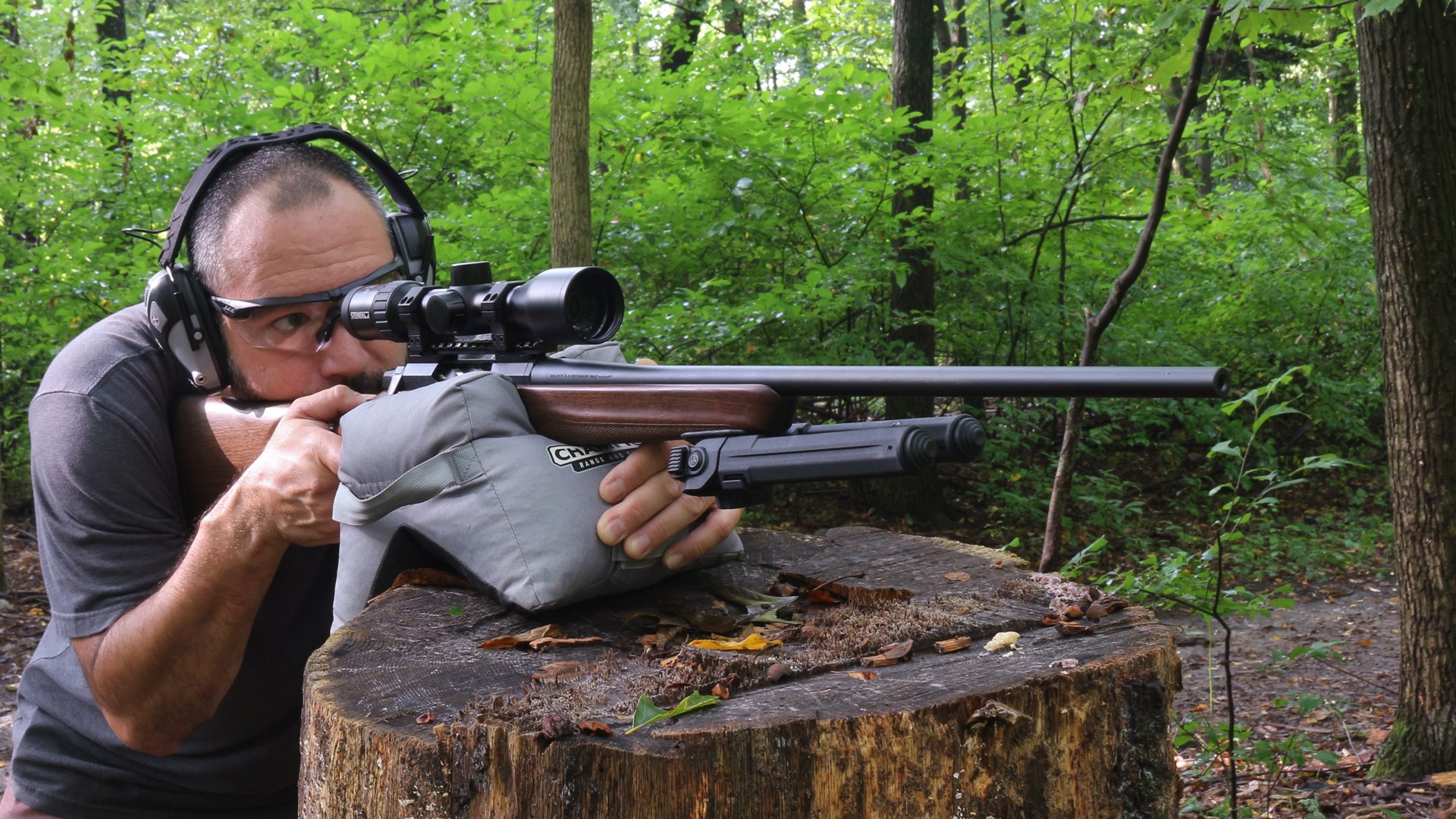 Man shooting the Browning X-Bolt 2 Hunter rifle off a sandbag rested on a tree stump in woods.