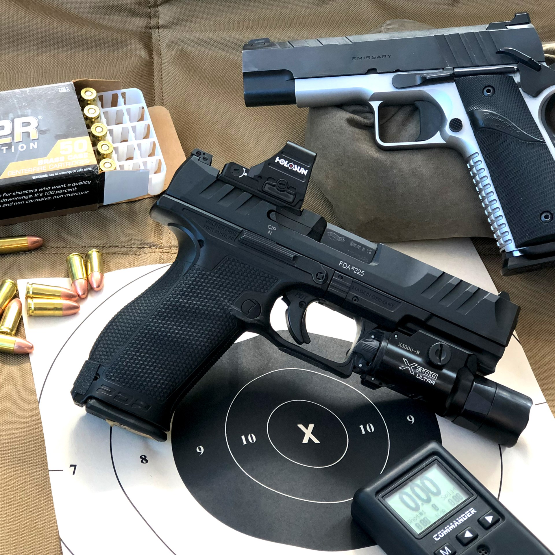 walther pdp pistol with holosun optic foreground emissary pistol 1911 background shown with bullseye target black circle X rings shot timer ammunition box rounds brass cartriges on green blanket mat shooting roll bag support