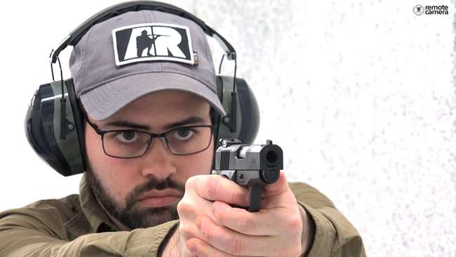 Man with gray hat and AR logo on white shooting range facing remote camera shooting a black-colored Armscor BBR pistol.