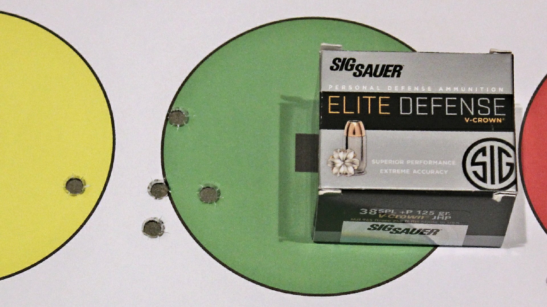 SIG SAUER ELITE DEFENSE ammunition box shown near green circle bullseye target with bullet holes signifying accuracy from Smith & Wesson revolver