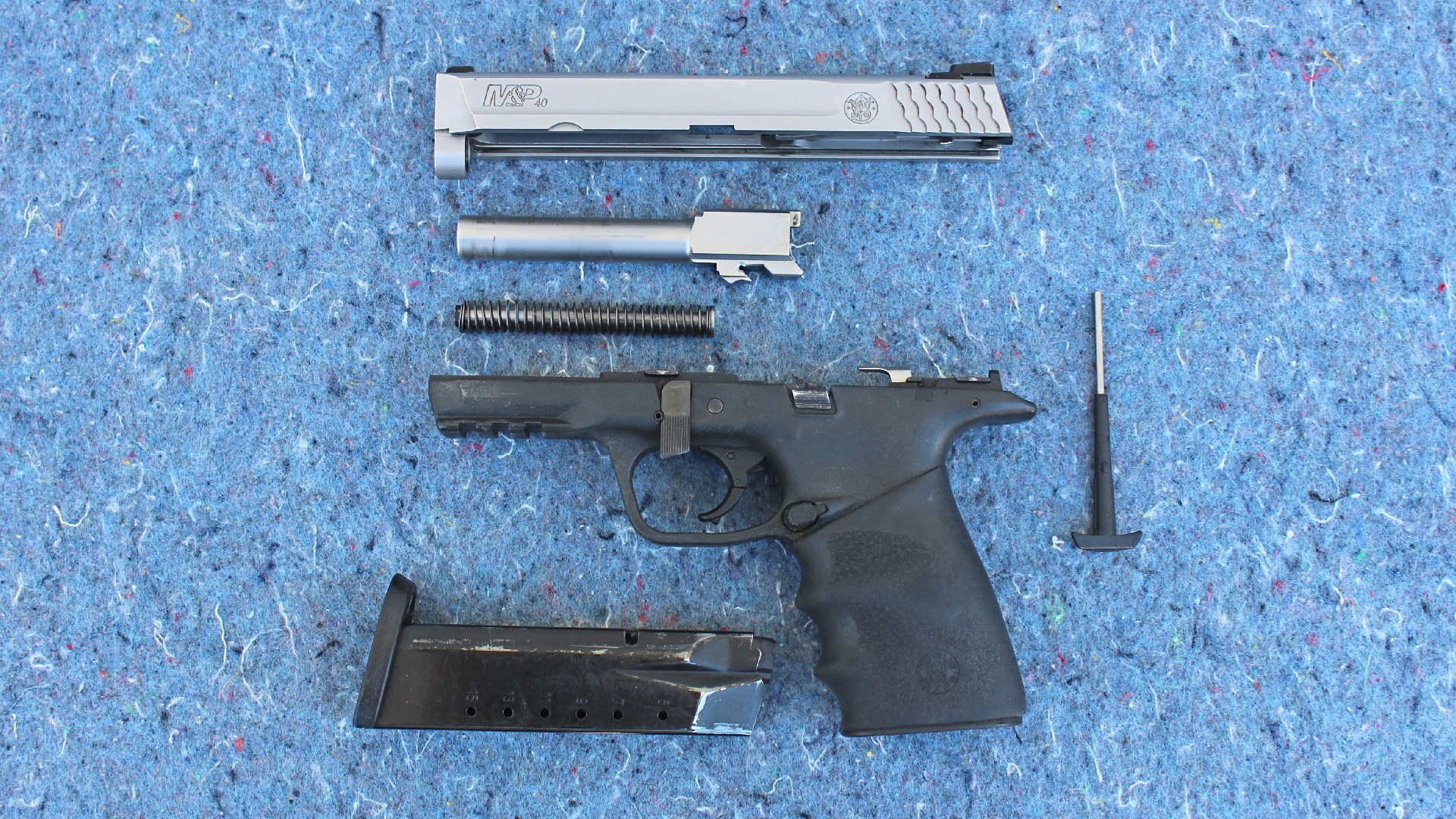 Exploded view of smith & wesson m&p 40 left-side view stainless steel slide barrel spring black polymer grip magazine blue background parts of gun