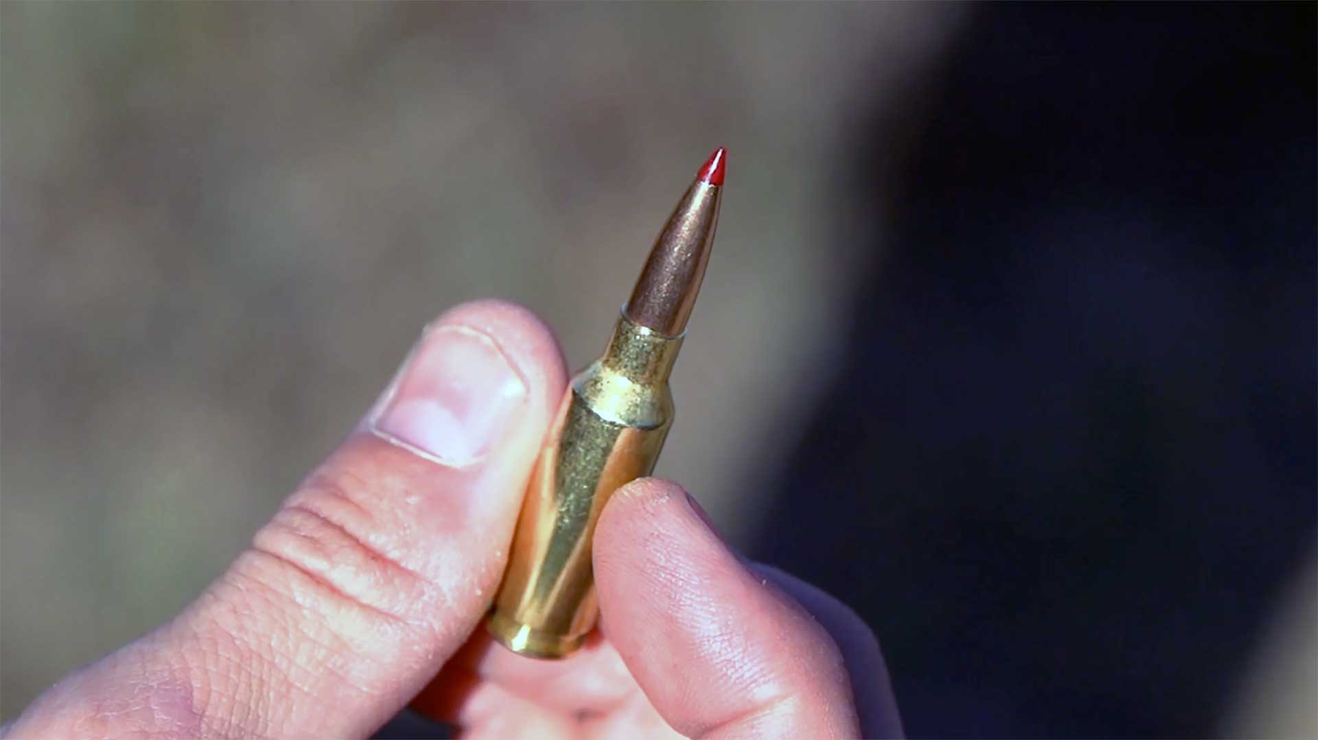 A man holding a Hornady 6mm ARC cartridge between his thumb and forefinger.