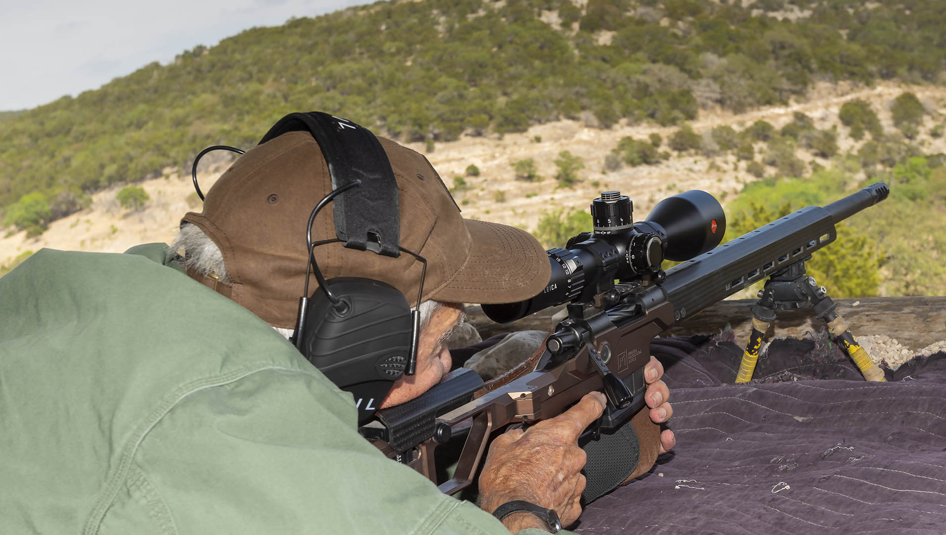 man behind rifle shooting long-range targets outdoors mountains hills