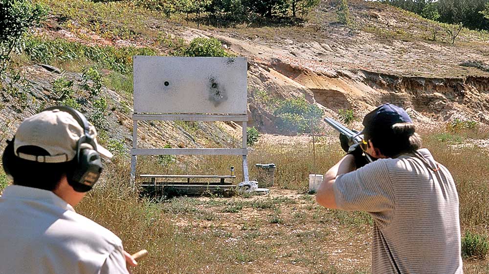 Two men outdoors shooting shotgun pattern board target white shotshell pellets impact group