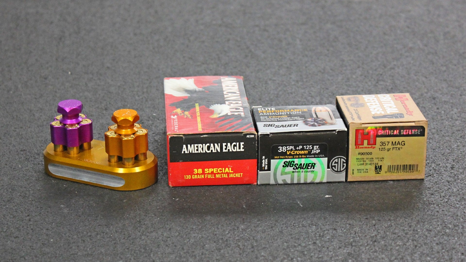 Three ammunition boxes sitting next to an orange anodized aluminum loading block.