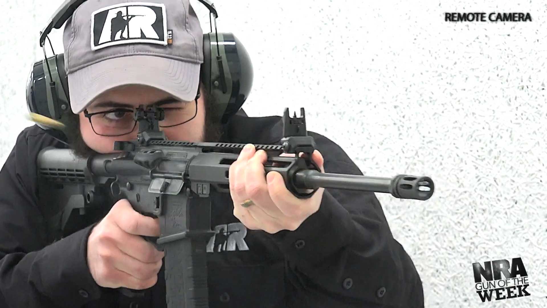 man in black shirt wearing ear muffs ballcap shooting rifle gun ar-15