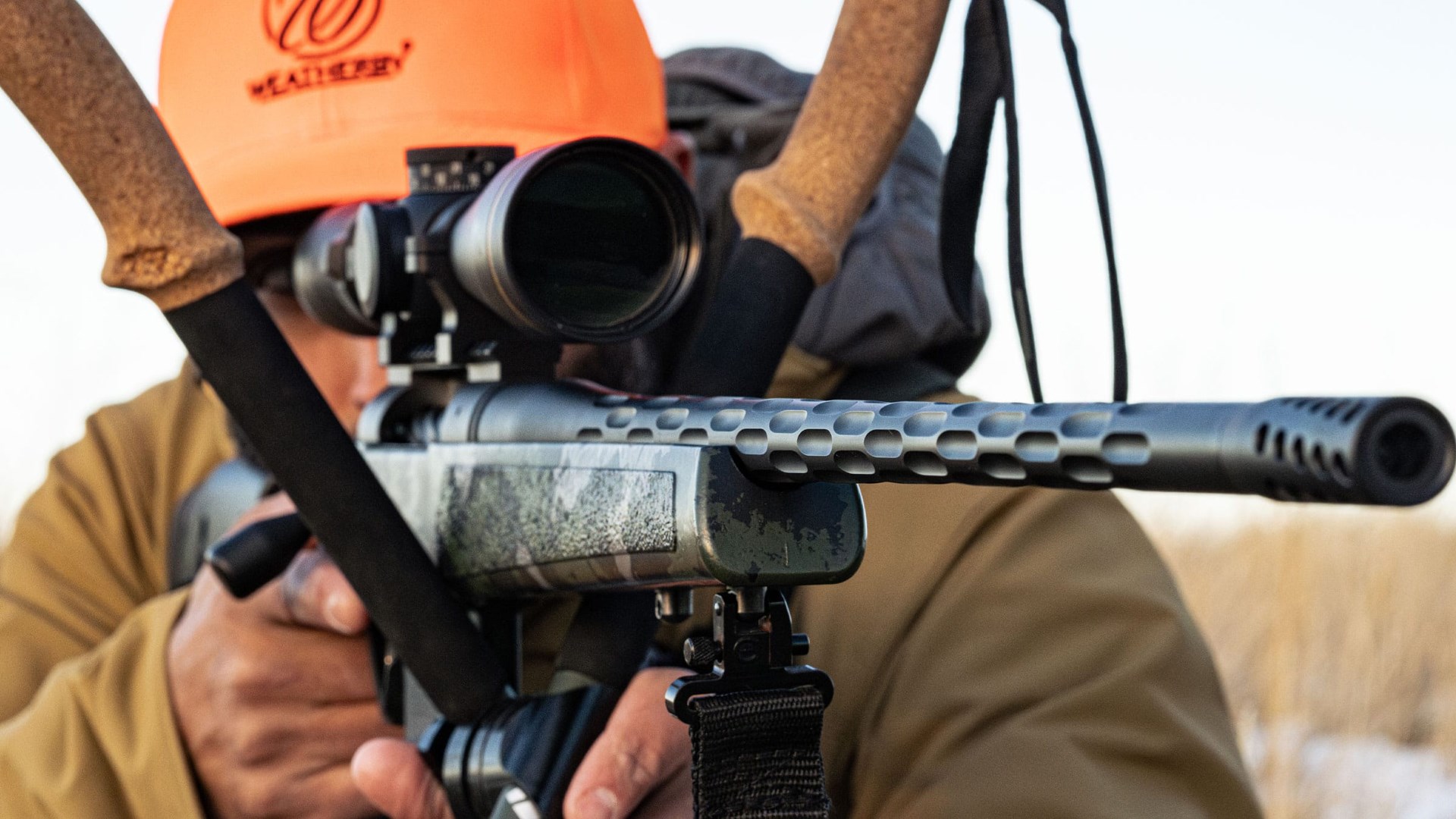 Man with orange hunting hat aiming a Weatherby Model 307 Range XP 2.0 rifle off hunting sticks.