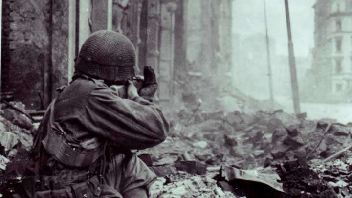 An armored infantryman of the 3rd Armored Division dismounted and fighting in the rubble of Cologne. He fires an M1 Carbine.