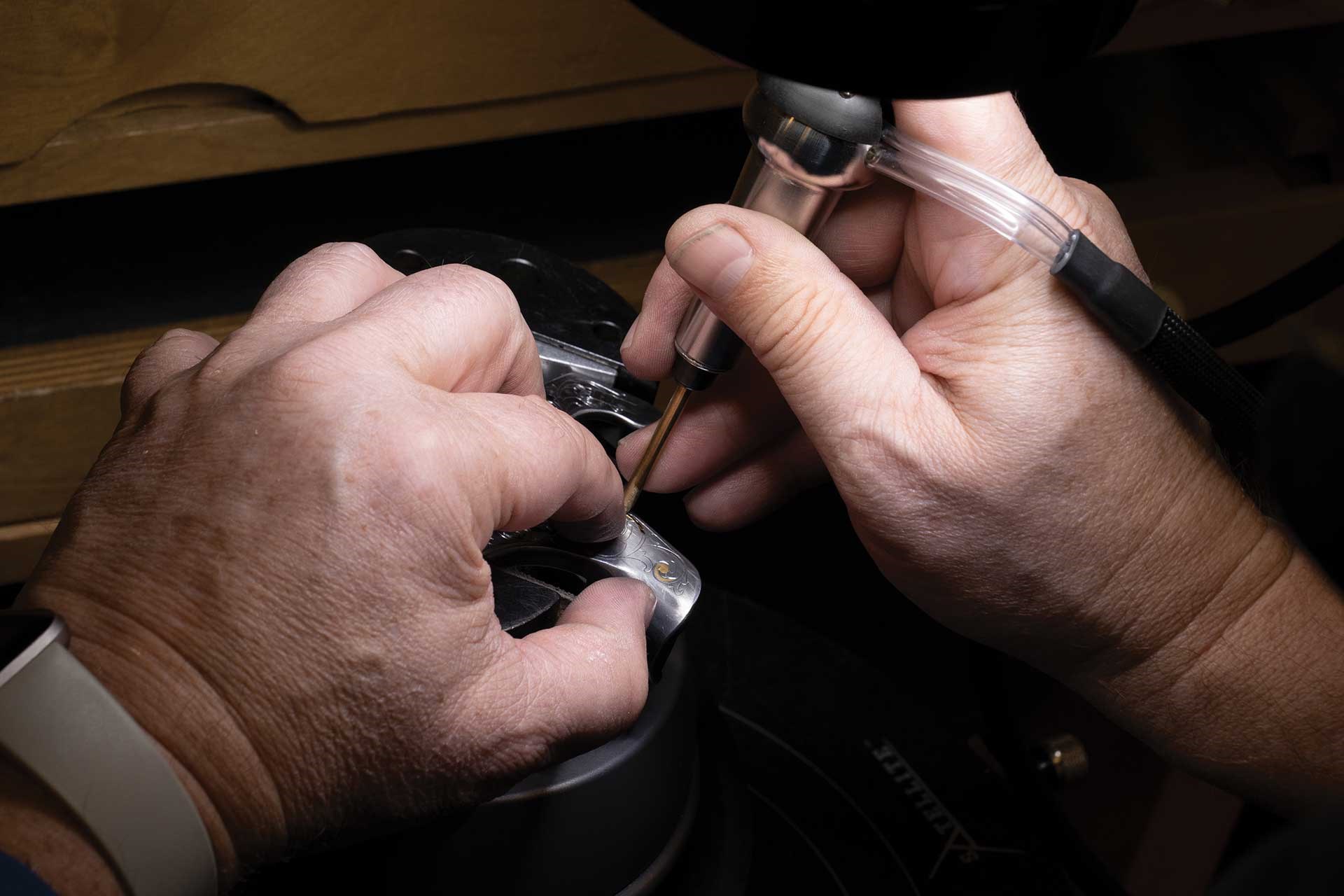 A man uses a specialized tool to engrave a firearm component.