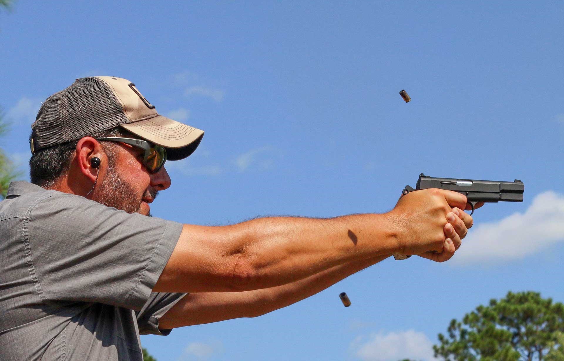 Man in gray T-shirt and baseball cap shooting the Springfield SA-35 High Power with multiple brass cartridge cases in the air.