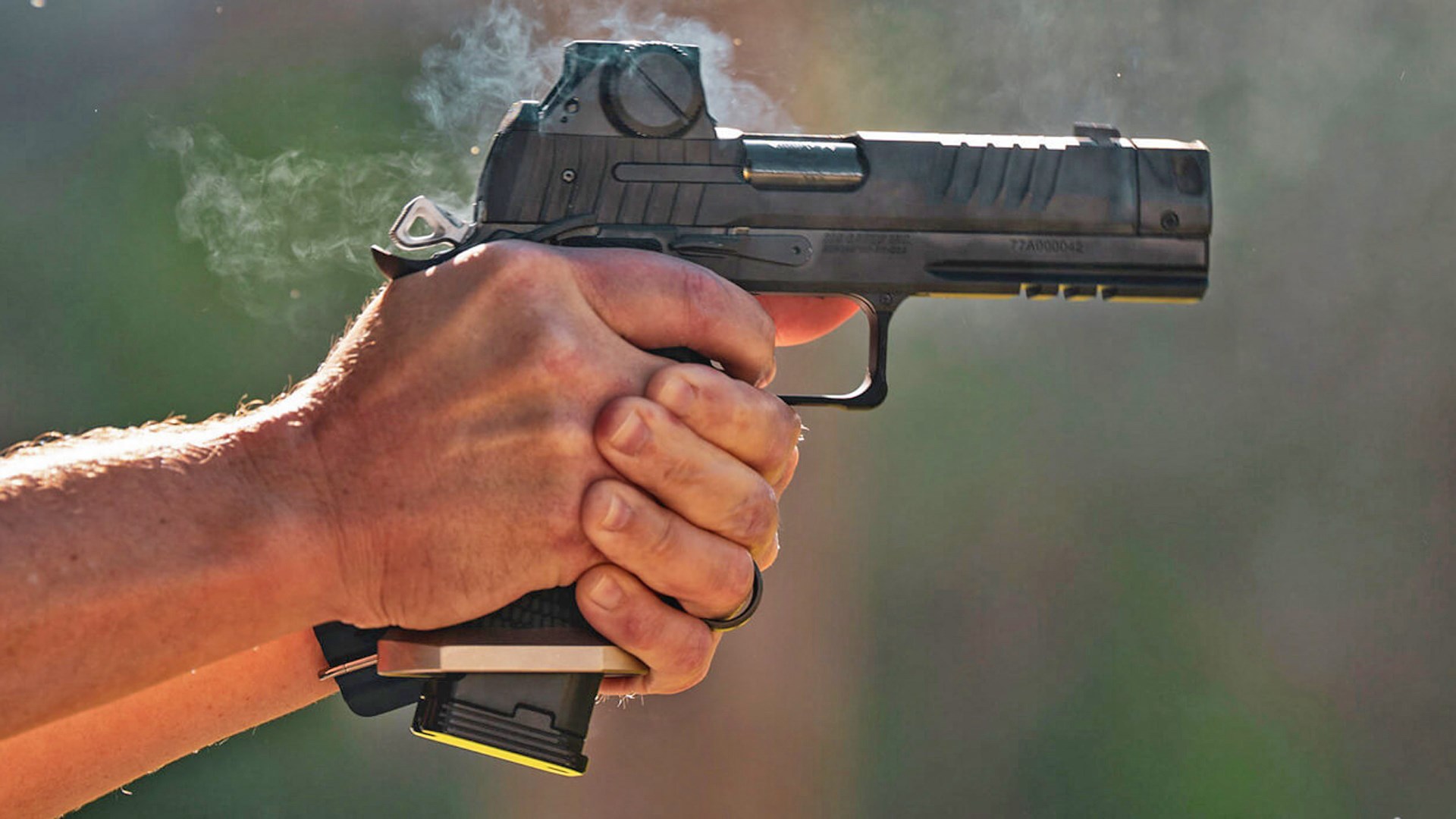 Man shooting a SIG Sauer P211-GTO pistol with smoke surrounding the gun.