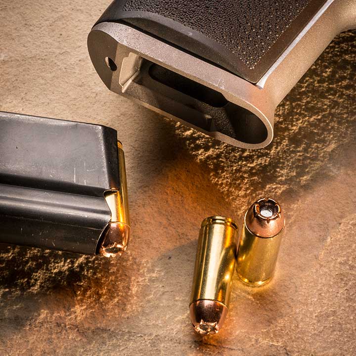 Magazine well of the Magnum Research Desert Eagle shown with the top of a loaded magazine resting on the side; two loose .50 AE rounds are laying on a sand background.