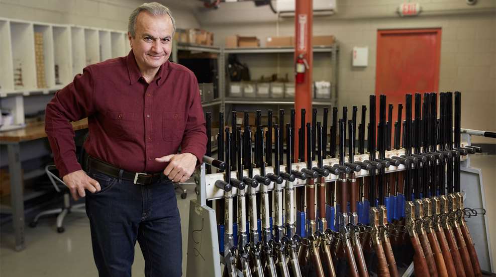 Man standing in room leaning on rack of guns rifles lever-action Henry Repeating Arms owner Anthony Imperato
