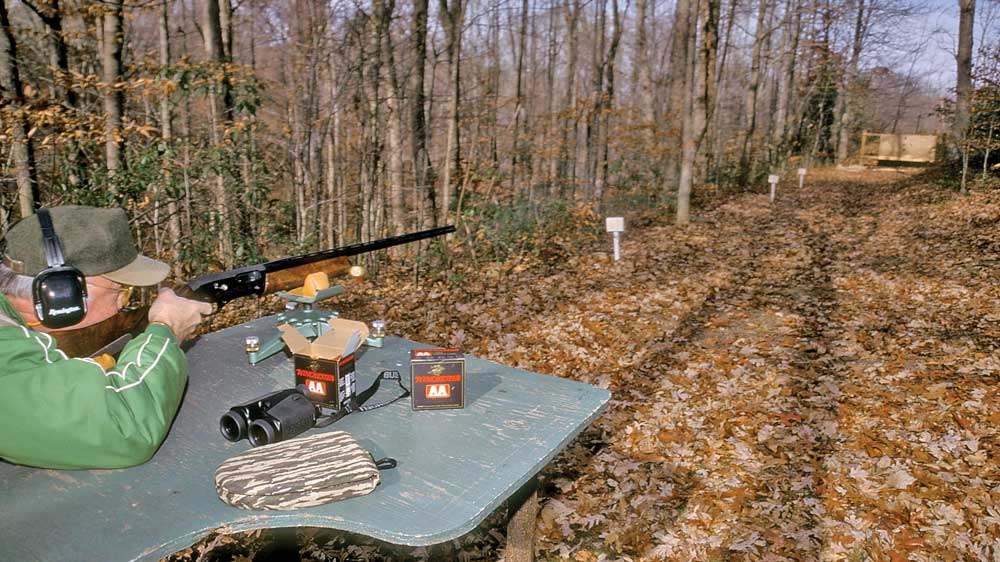 Man sitting at shooting bench outdoors woods fall winter leaves shooting range shotgun patterning