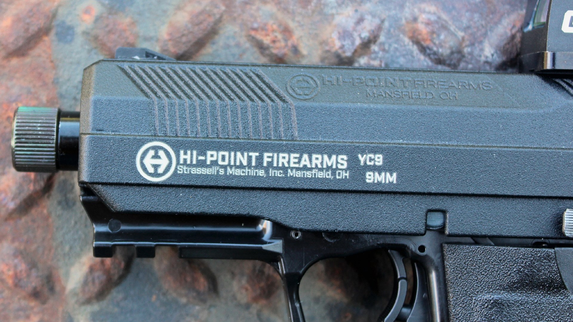 Hi-Point Firearms YC9 9mm stamping closeup strassell's machine inc. mansfield ohio gun slide black powdercoat alloy yeet threaded barrel crimson trace red-dot rust netal background