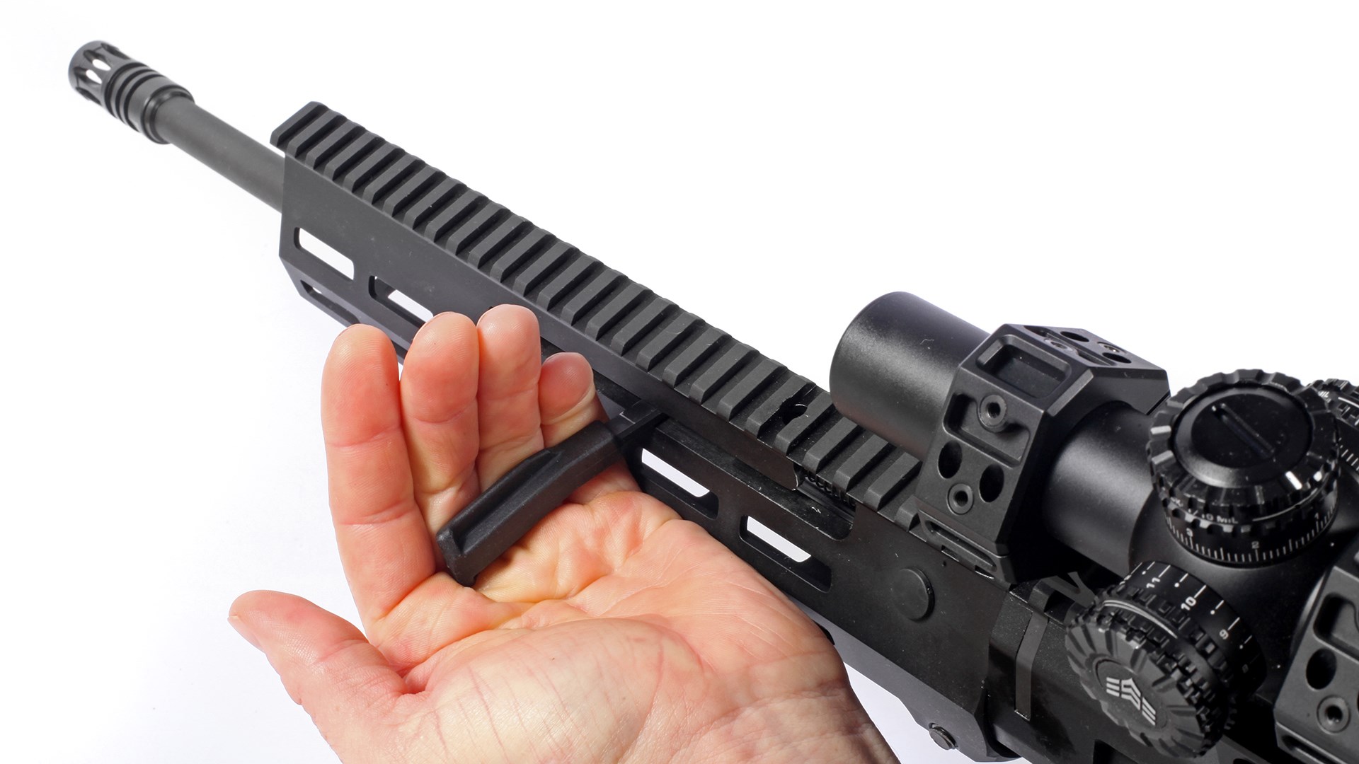 Zenith Firearms charging handle within handguard with Picatinny rail grasped by and shown on white with partial view of riflescope
