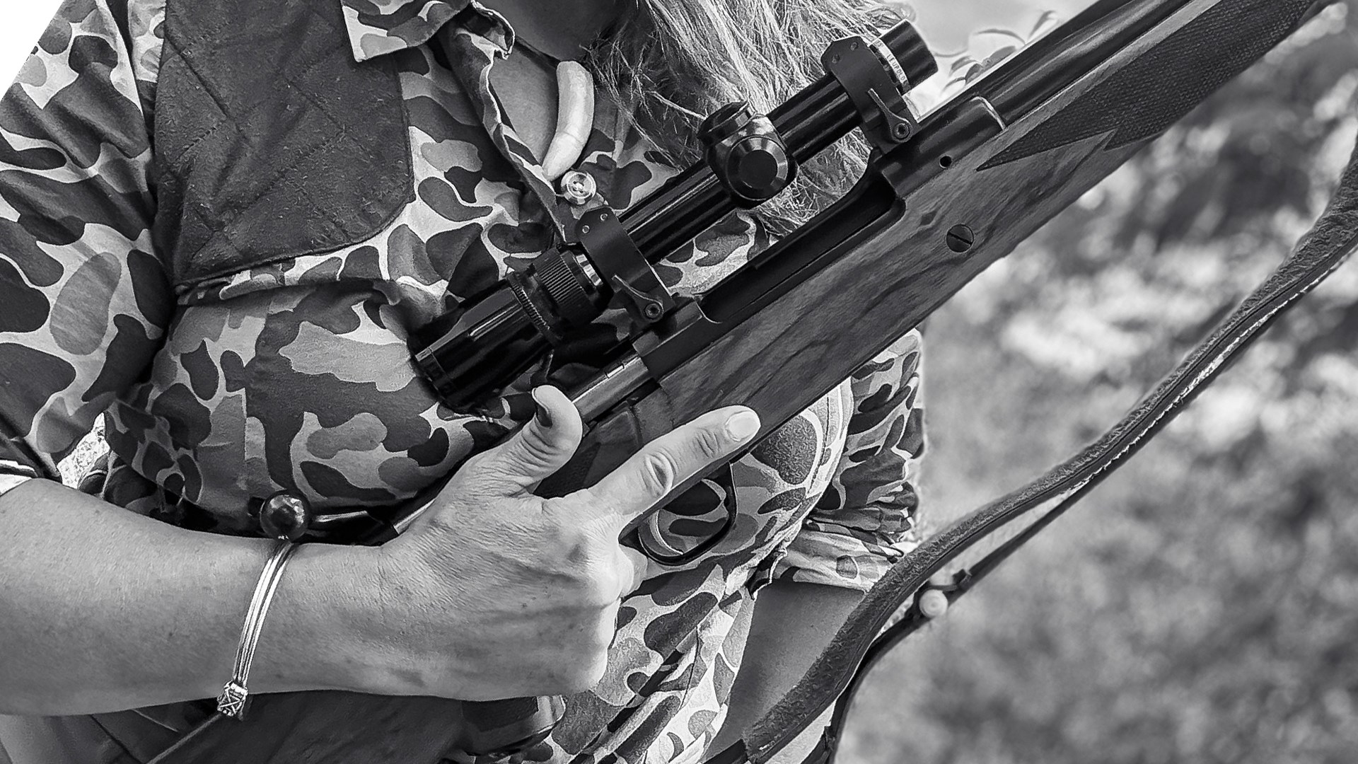 Black and white photo of huntress wearing camouflage outdoors holding bolt-action rifle controlled-round-feed mauser-style rifle finger point off trigger