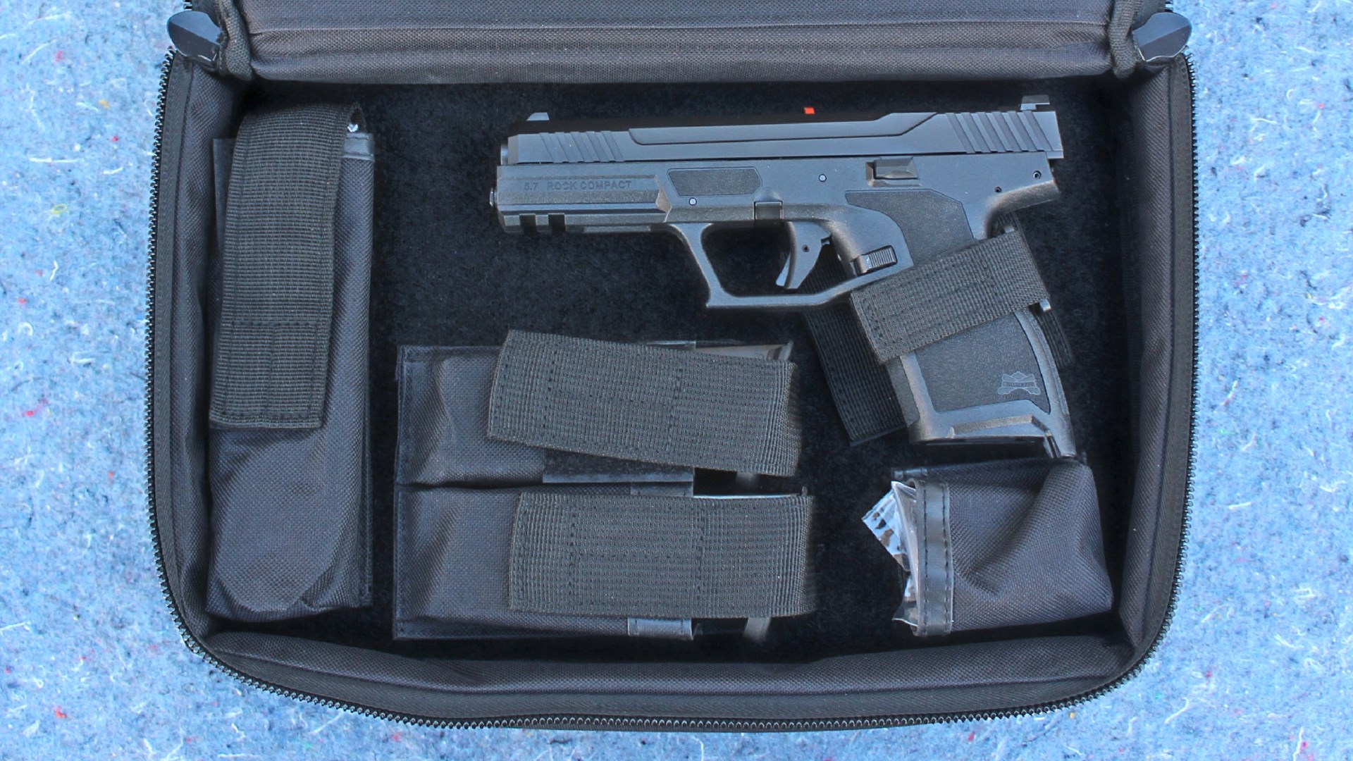 Palmetto State Armory 5.7 Rock Compact pistol in zipperd nylon case hook and look straps compartments pouches magazines chipped blue stone background