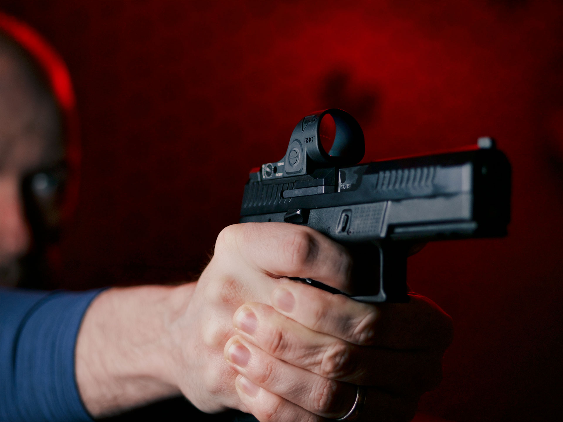Shooter standing in front of a red background, aiming a handgun downrange.