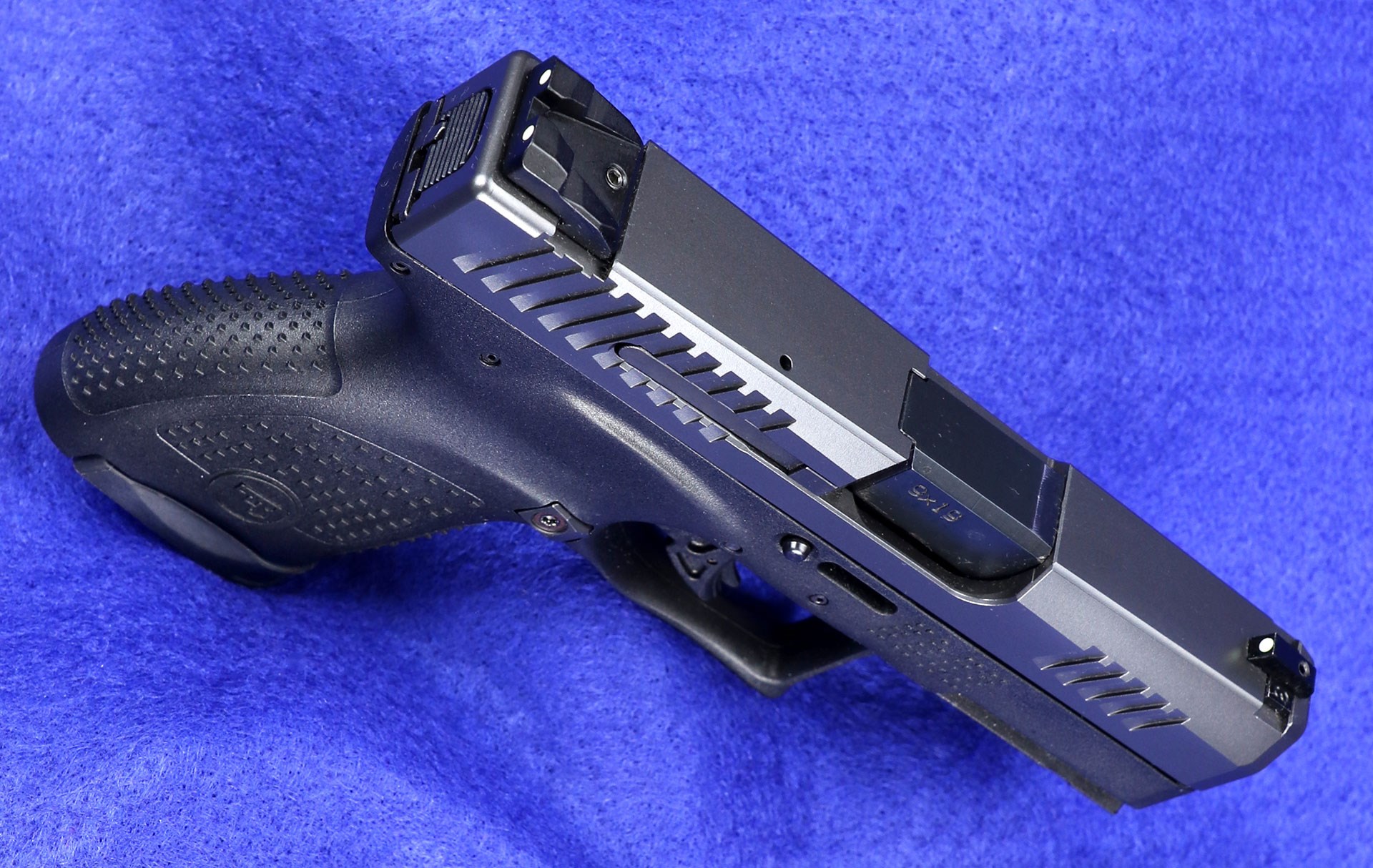 an overhead view of the CZ P-10 M on blue background, overhead view showing white three-dot iron sights.