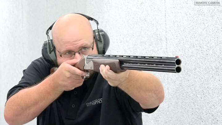 Man wearing protective gear and black shirt shooting a shotgun.