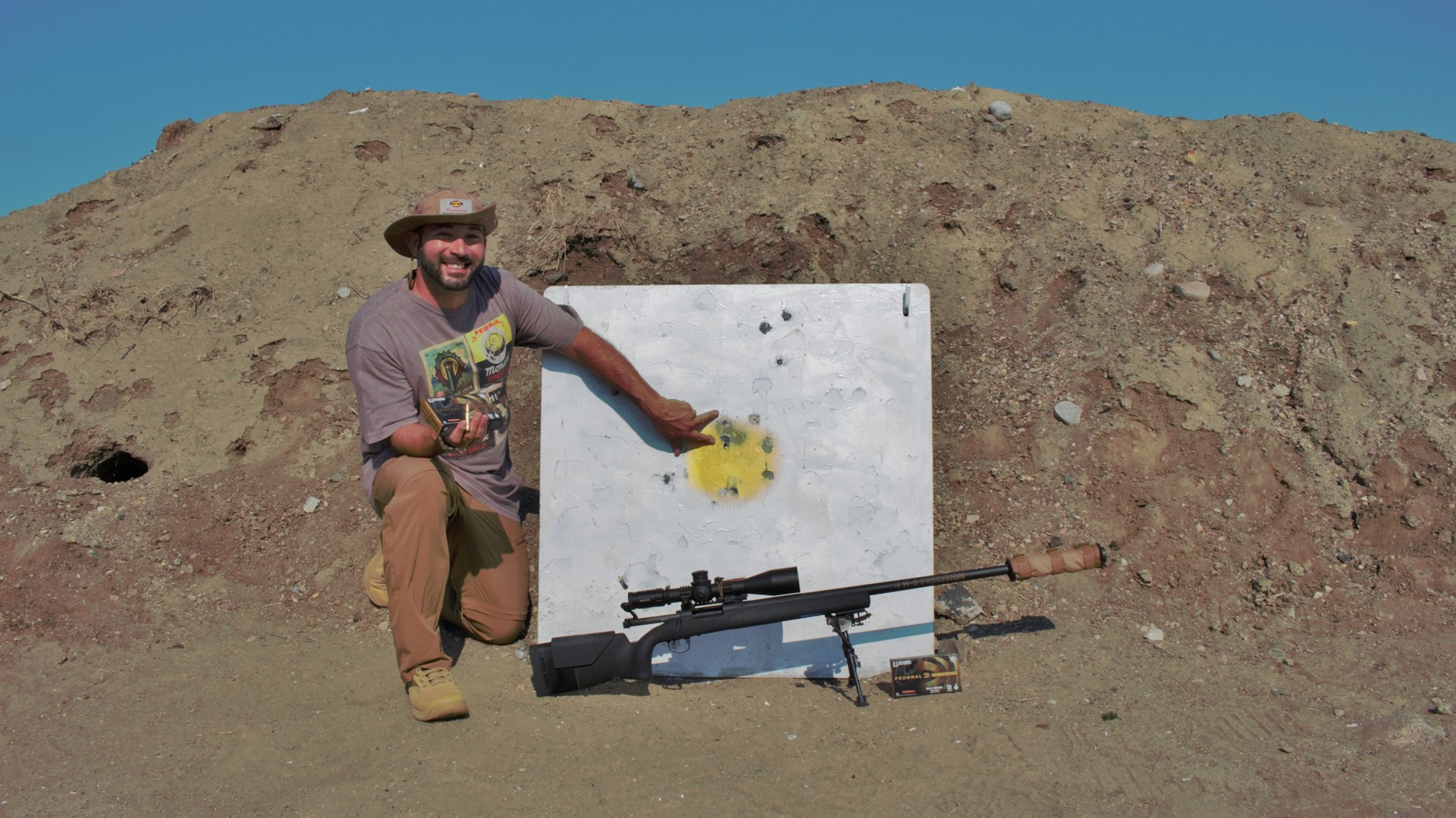 Author Frank Melloni knelt next to white square target one-mile with rifle bolt-action hill behind blue sky