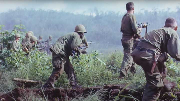 American soldier cautiously mover forward through vegetation in Vietnam.
