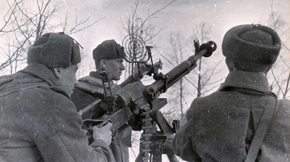 heavy machine gun crew with DShK on tripod pointing in air above trees