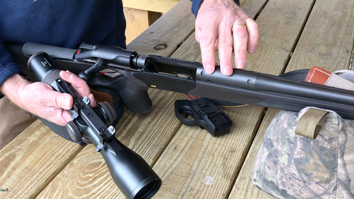 A rifle on a bench in the hands of a man installing an optic.