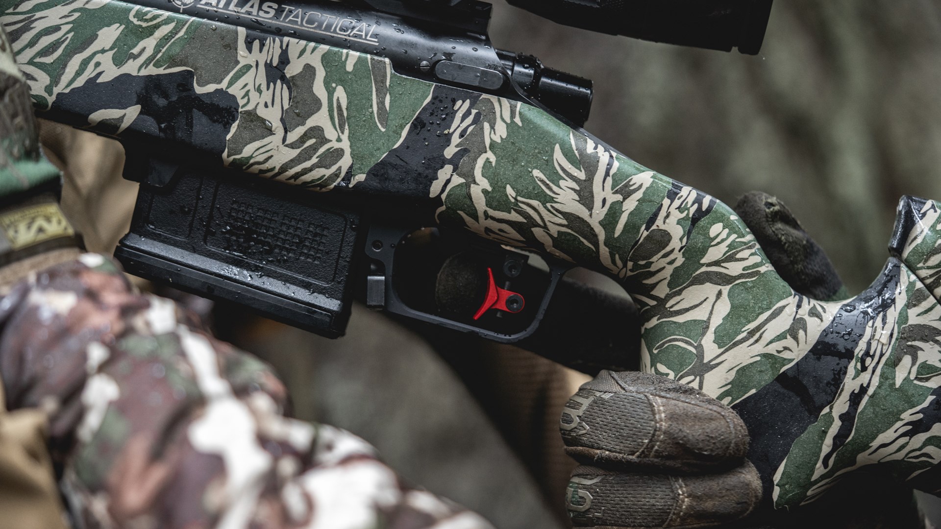 Left-side view of camouflage atlas bolt-aciton rifle with focus on timney calvin elite adjustable two-stage trigger red highlight