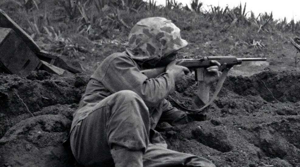 U.S. soldier sitting against dirt bank hillside fighting with m1 carbine on shoulder