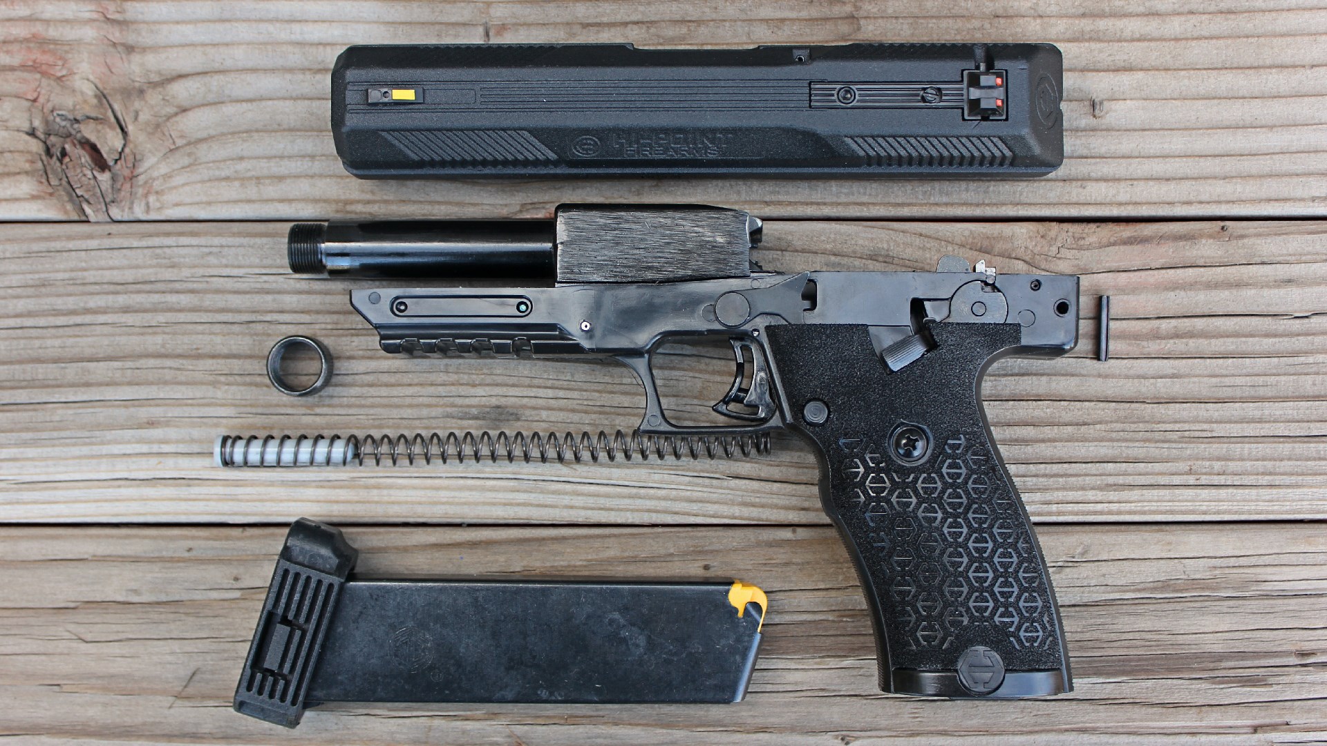 Disassembled view of Hi-Point JXP 10 left side slide barrel spring magazine pistol frame shown on wood boards