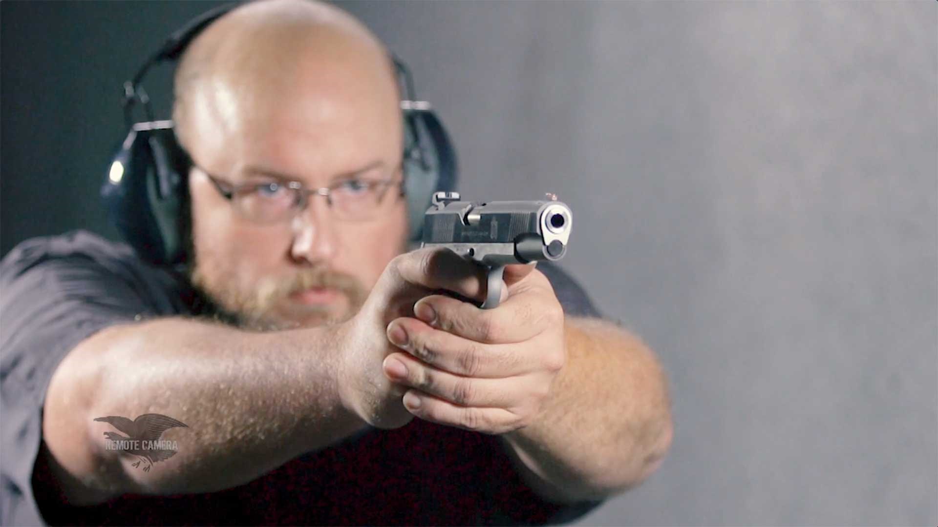 A man aiming a Springfield Armory Ronin 1911 on an indoor range with white walls.
