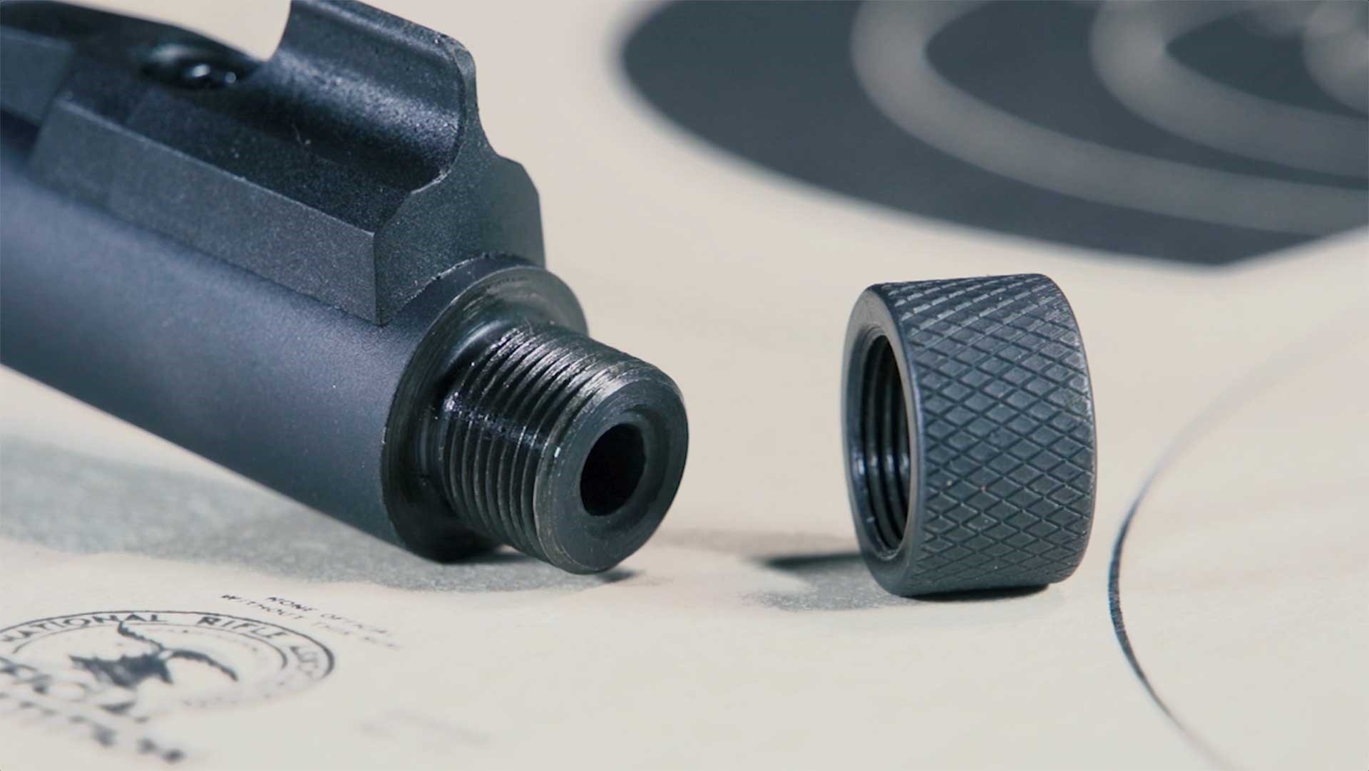 The threaded muzzle and black thread protector of the Winchester Wildcat 22 SR shown on top of an NRA bullseye target.