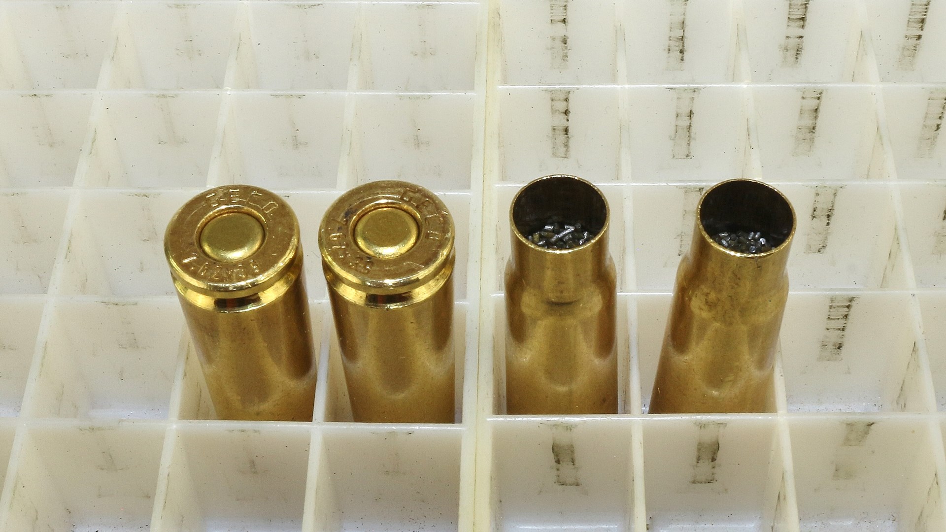 four cartridge ammunition brass cases in tray cubical organizer two cases pointing down and two cases pointing up with gunpowder inside