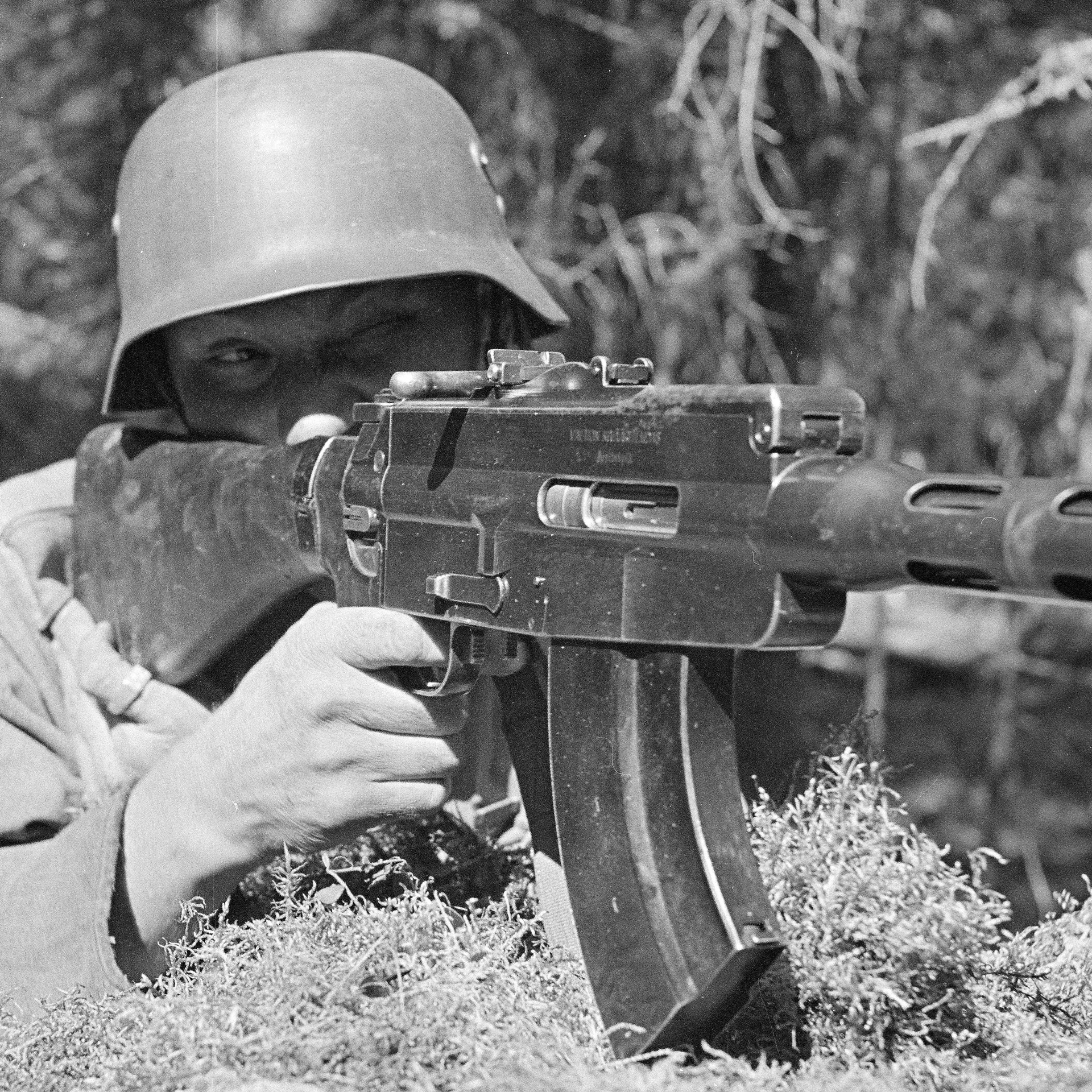 M/26 light machine gun finish soldier aiming outdoors curved magazine right-side angled view trees background