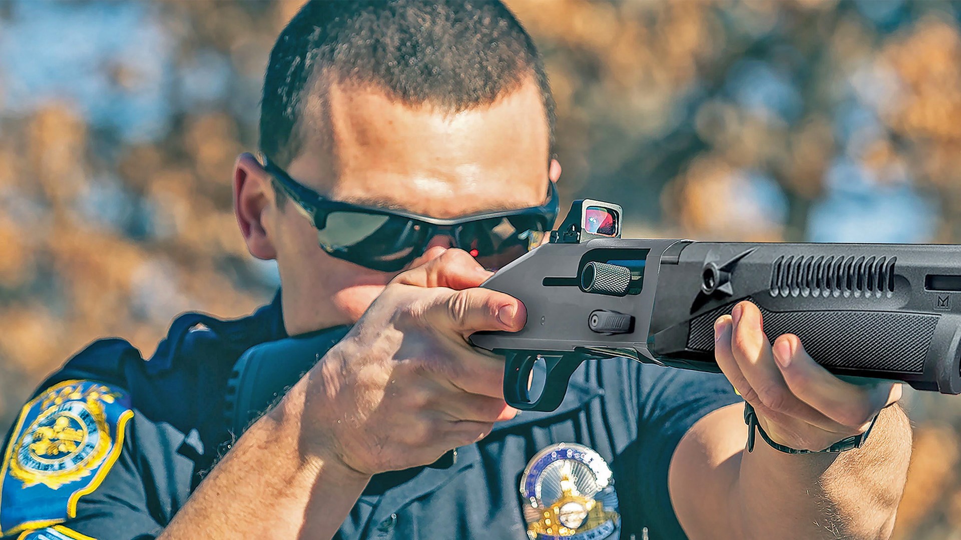 Law enforcement officer wearing sunglasses and aiming a Mossberg 940 Pro Tactical Professional Series shotgun.