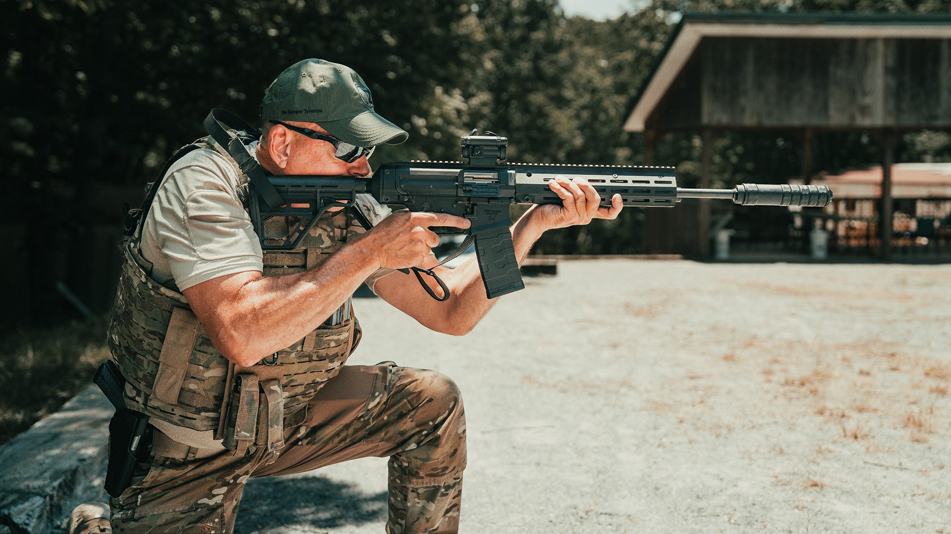 Man in camouflage kneeling holding rifle outdoors