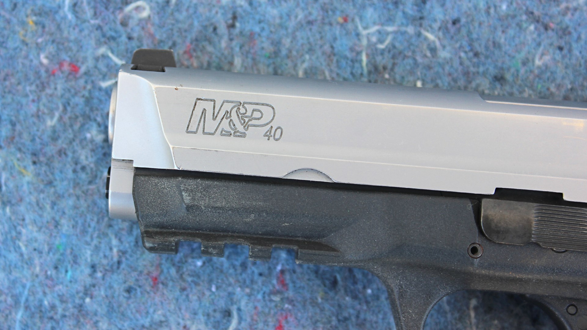 Smith & Wesson M&P 40 stainless steel slide closeup of muzzle barrel front sight and dustcover of gun pistol left-side view on blue background