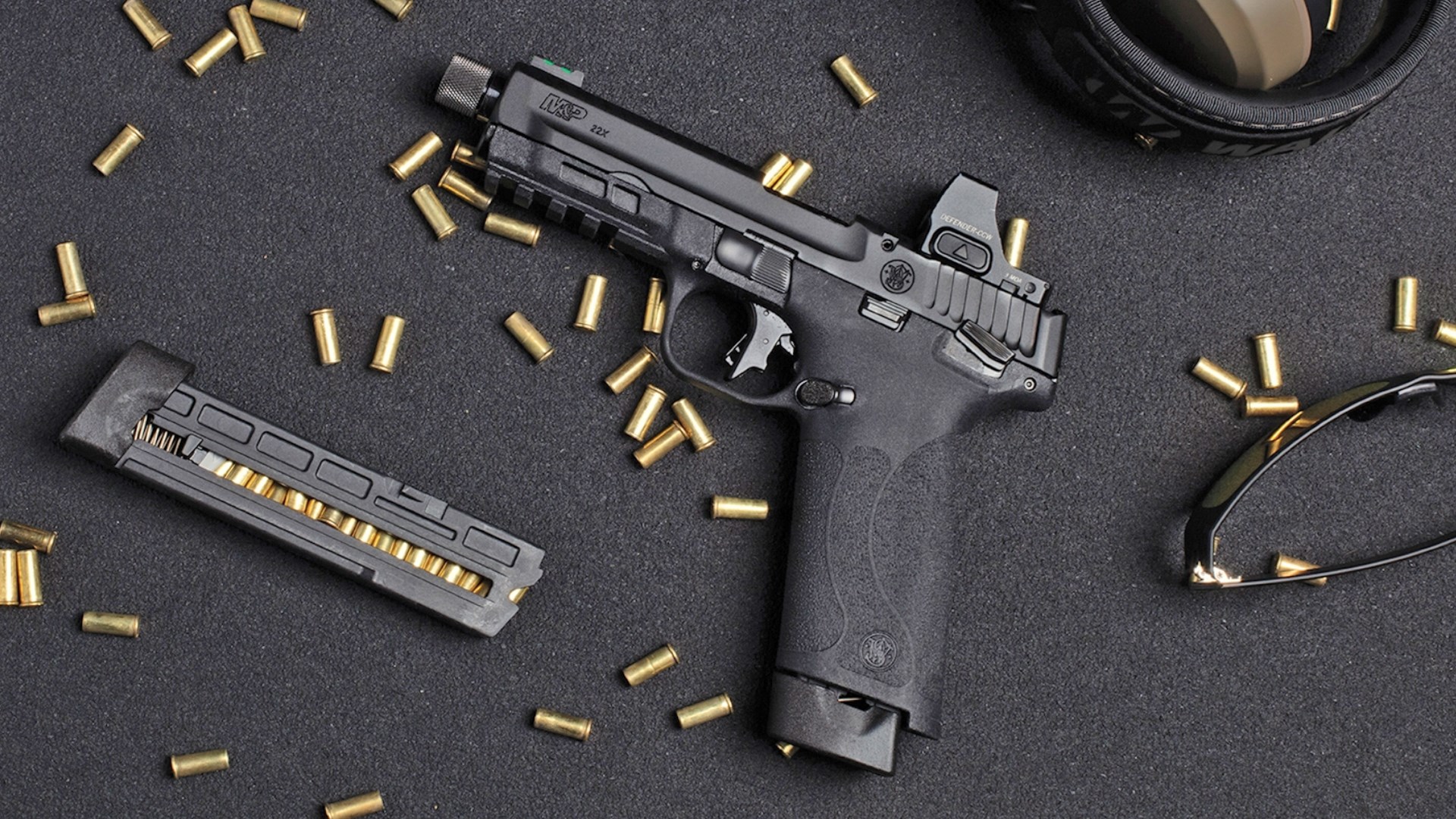 Left side of the M&P 22X lying on a black table, surrounded by spent cartridge cases.