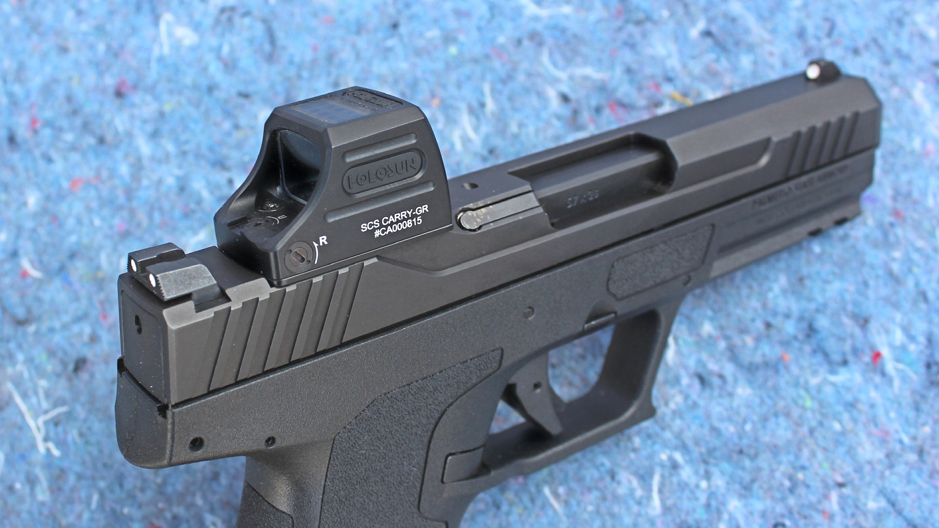 Holosun optic attached to top of black-colored Palmetto State Armory 5.7 Rock Compact pistol blue background
