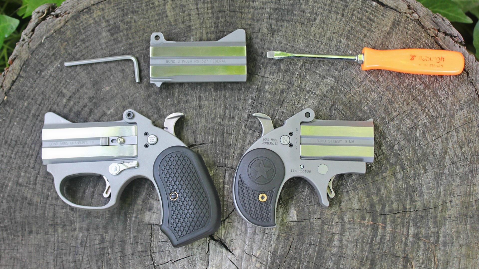 Two Bond Arms derringers resting on a tree stump next to a screwdriver and a spare barrel.
