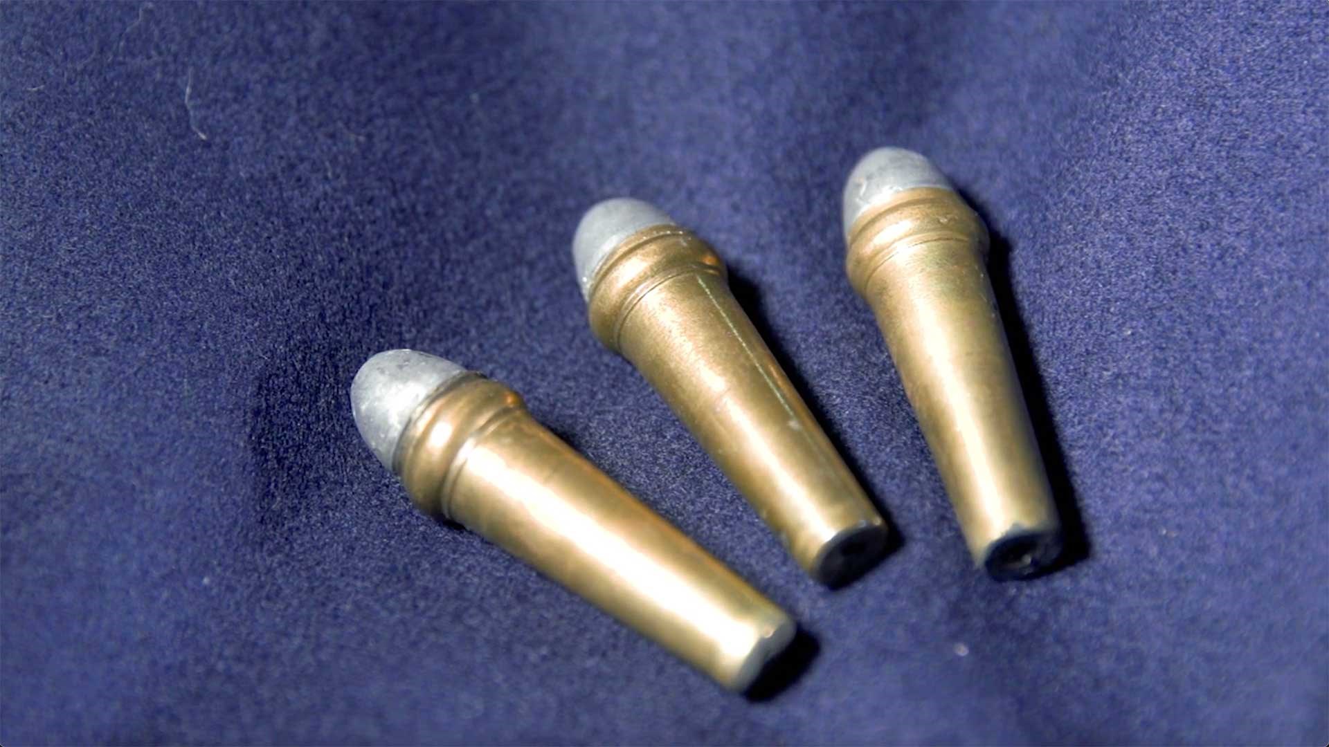 Three Burnside carbine cartridges laid out on a blue cloth background.